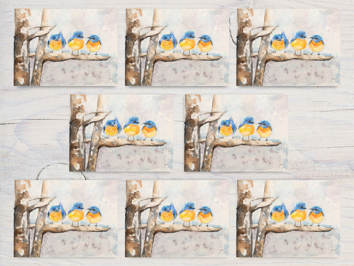 A repeating pattern of square art prints arranged on a light wood background. Each print shows four small bluebirds with yellow bellies perched on a birch branch against a pale winter sky.