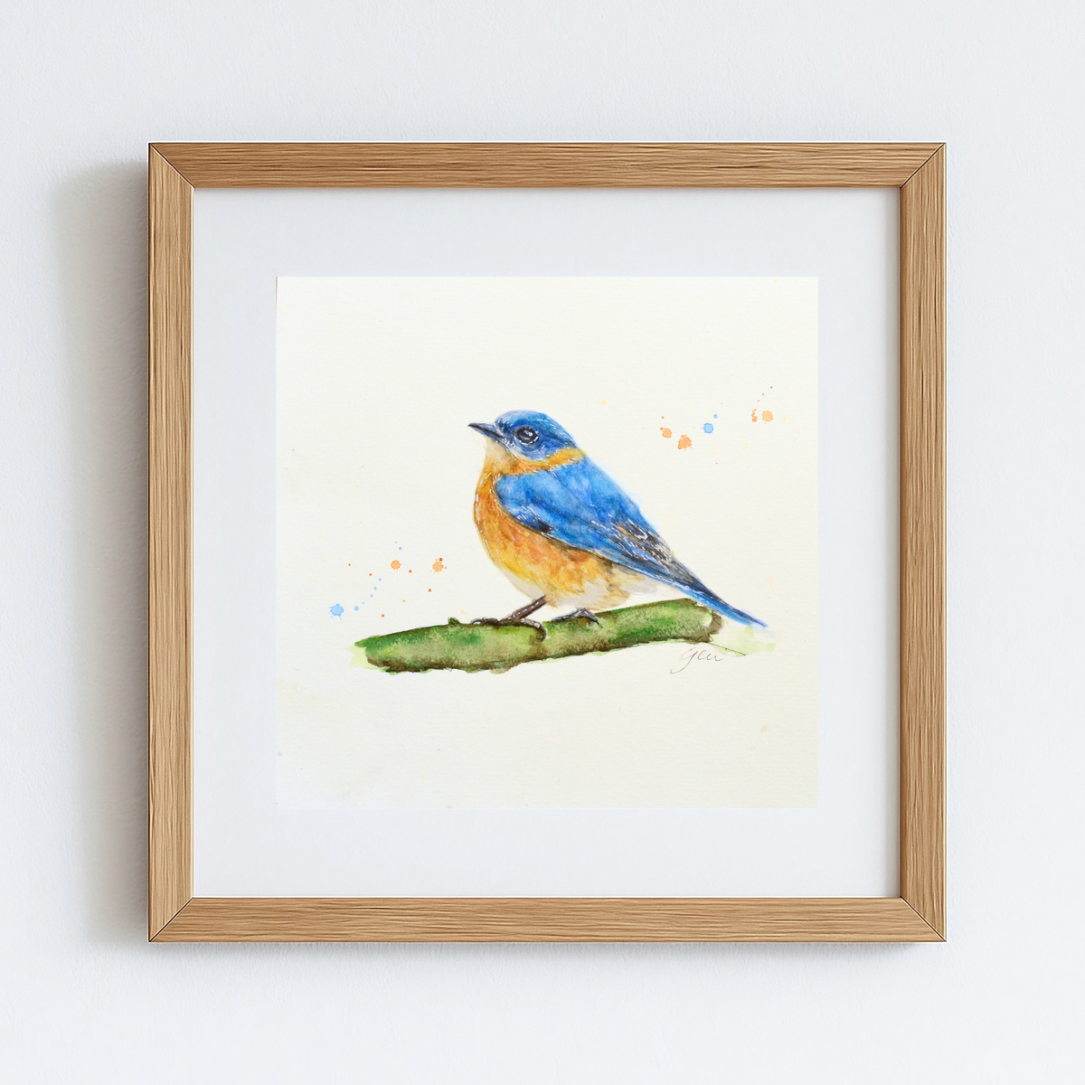 A framed watercolor painting of a bluebird perched on a green branch, set against a white mat and a light natural wood frame, hanging on a white wall.